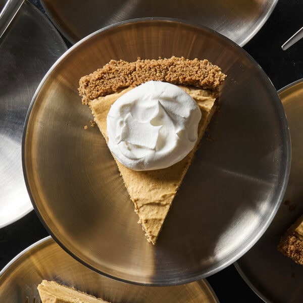 Silver plate with slice of frozen pumpkin cheesecake with dollop of whipped cream.