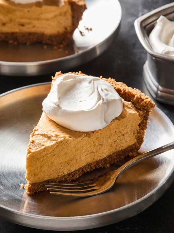 Silver plate with slice of frozen pumpkin cheesecake topped with whipped cream.