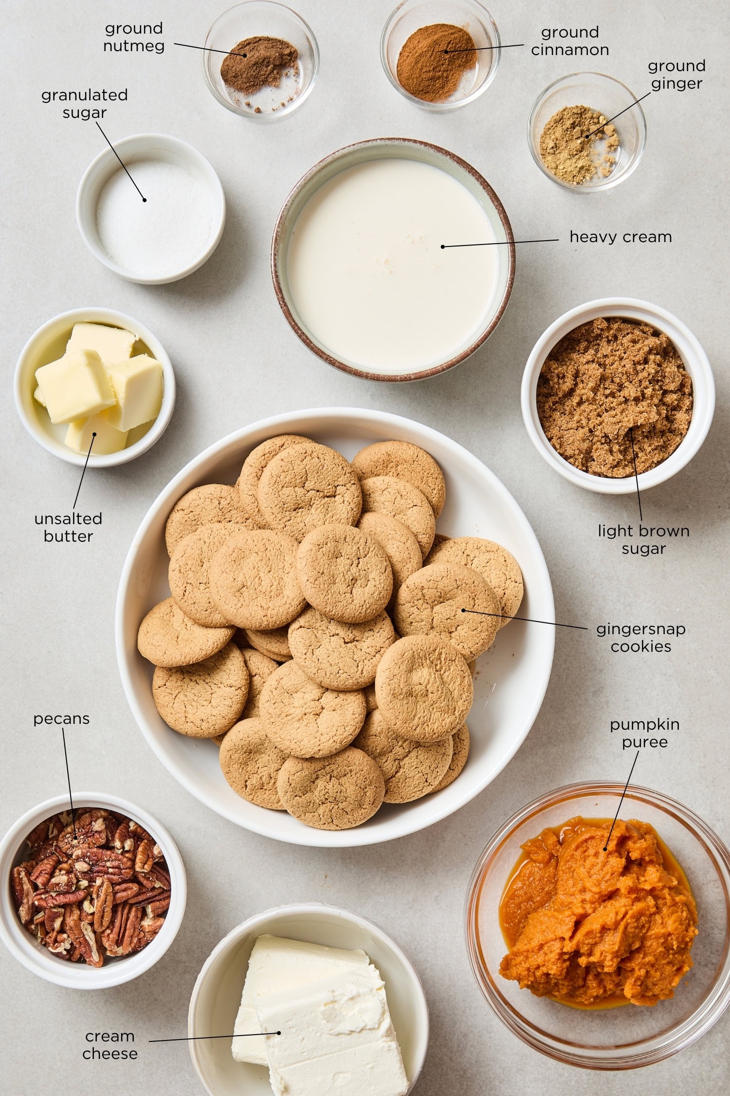 Concrete surface filled with ingredients for frozen pumpkin cheesecake including gingersnaps, sugar, pecans, pumpkin puree, and more.