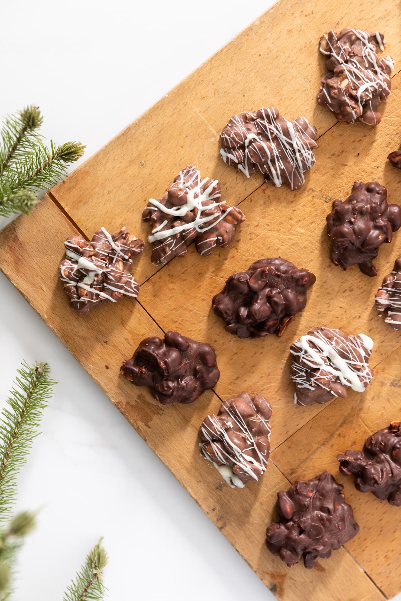 Top down view of wood board sitting on white surface with chocolate globs, some drizzled with white chocolate streaks