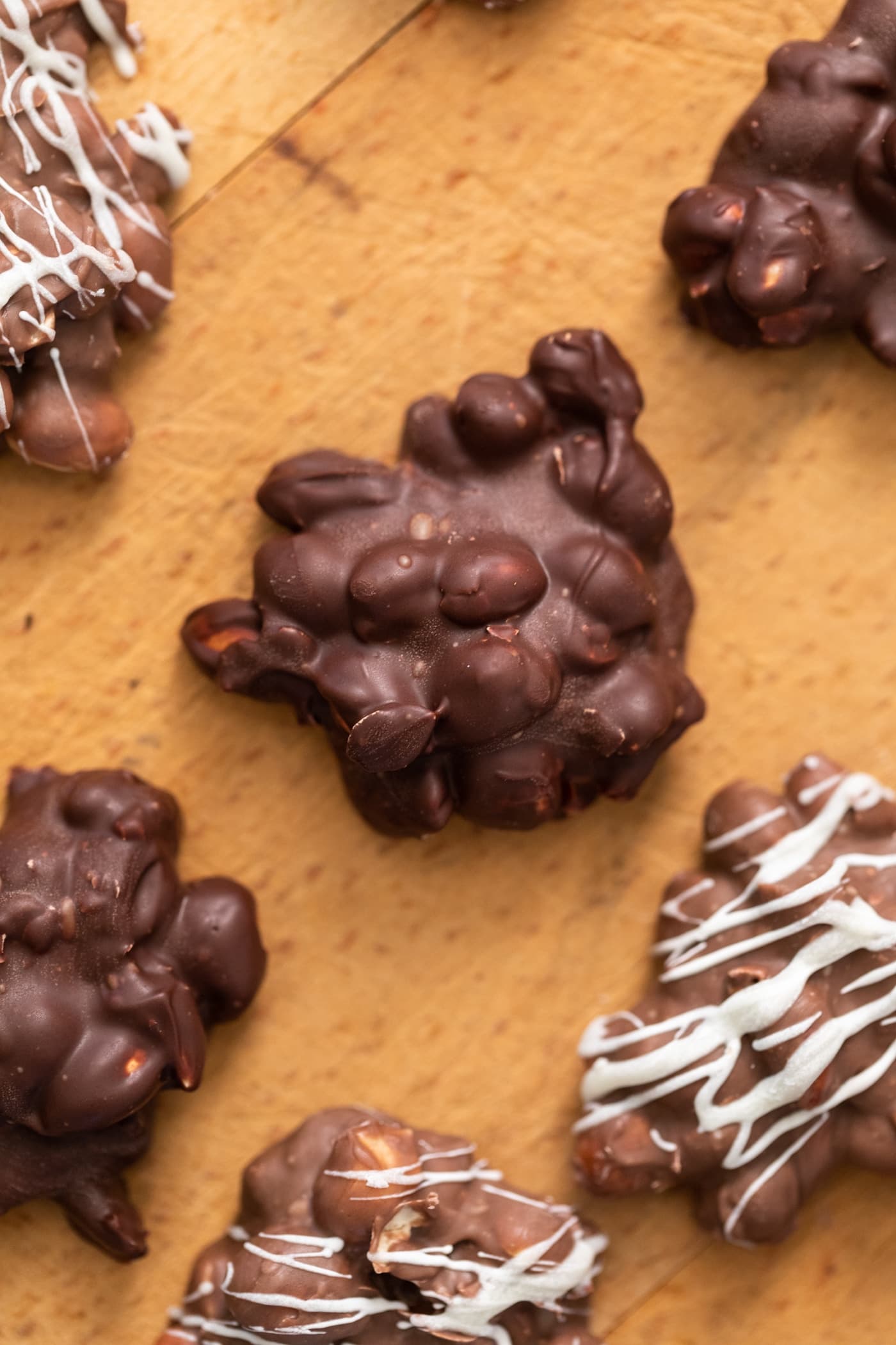 Dark chocolate peanut cluster sitting on wood surface surrounded by other chocolate clusters
