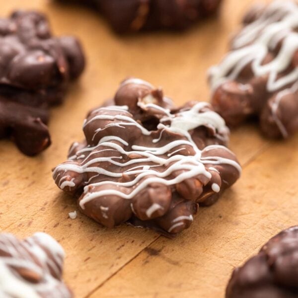 Chocolate peanut clusters topped with white chocolate sitting on wood surface