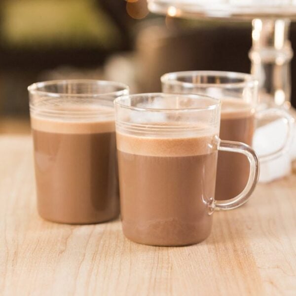 Small glasses of sipping chocolate resting on a wooden surface with peppermint marshmallows in the background.