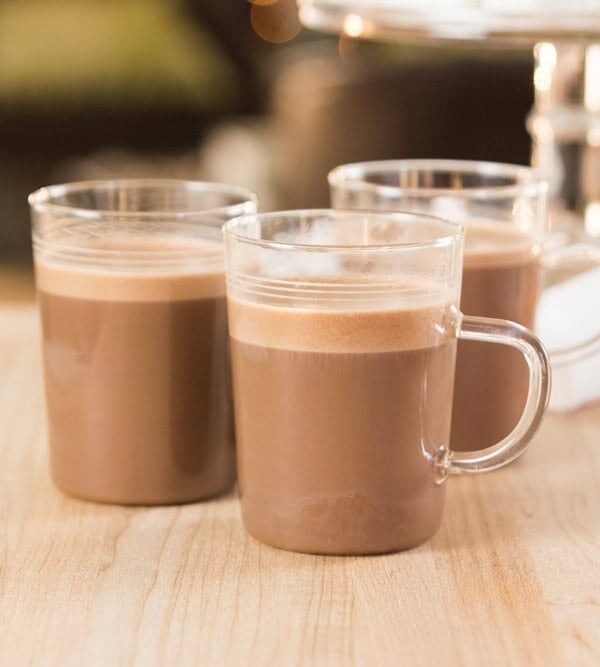 Small glasses of sipping chocolate resting on a wooden surface with peppermint marshmallows in the background.
