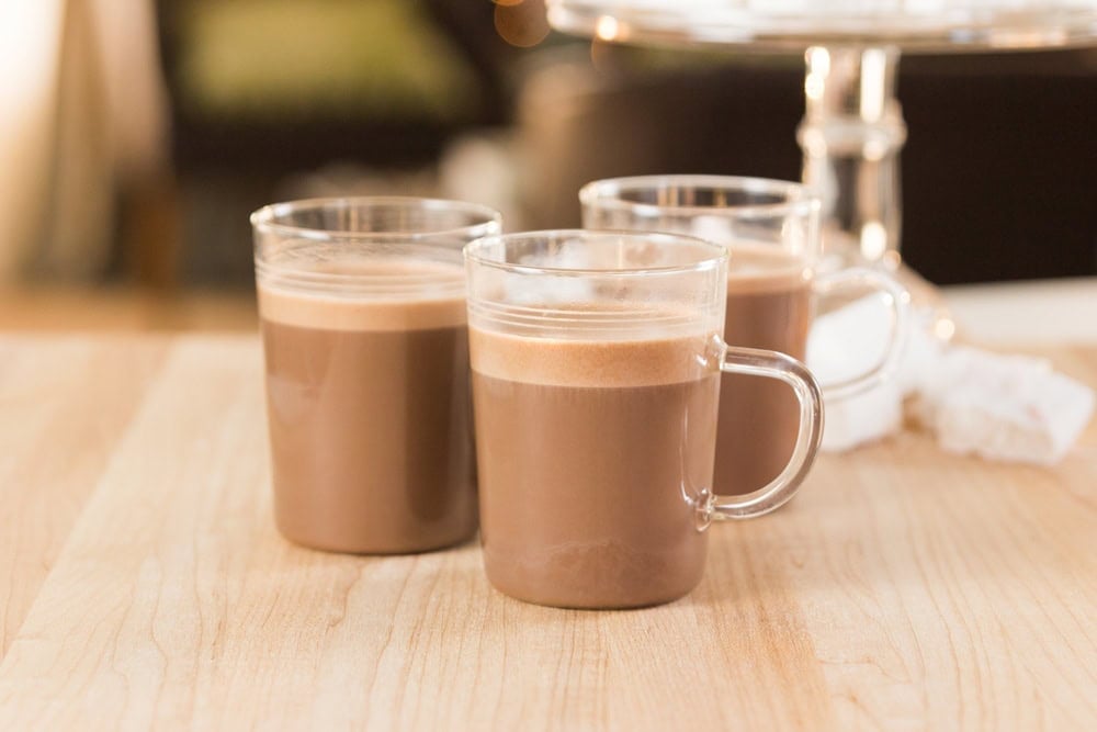 Small glasses of sipping chocolate resting on a wooden surface with peppermint marshmallows in the background.
