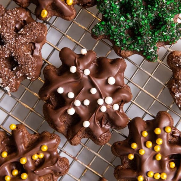 Top down view of chocolate waffle cookies sitting on wire cooling rack on white countertop with the cookies topped with dragees and sanding sugar