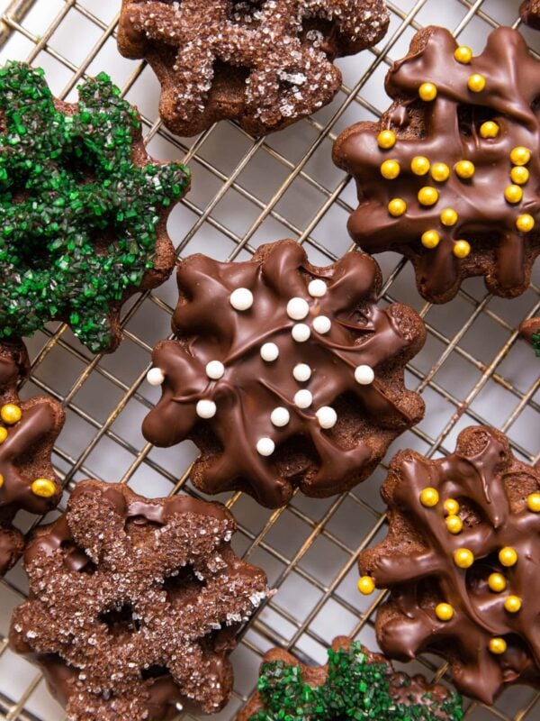 Chocolate waffle cookies sitting on wire cooling rack with lots of decorations on top including white dragees and green frosting