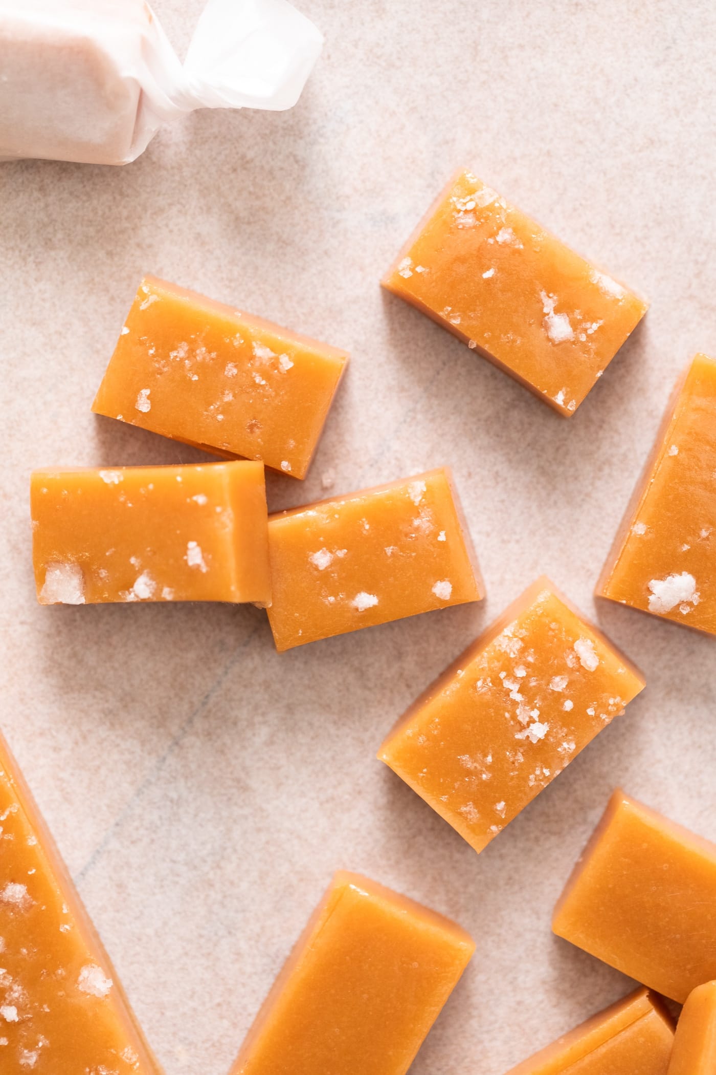 Top down view of pieces of caramel, some with sea salt on top, sitting on white piece of parchment