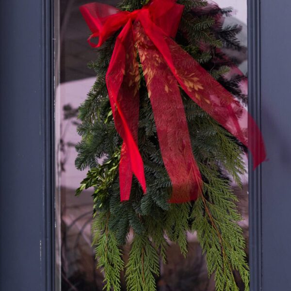 Greenery bundle attached to a front door with a wispy red ribbon adorning the top.