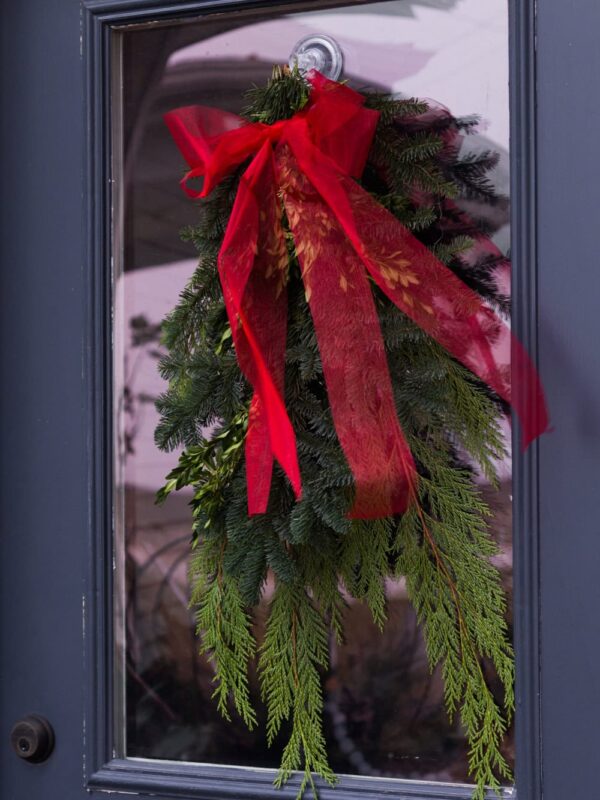 Greenery bundle attached to a front door with a wispy red ribbon adorning the top.