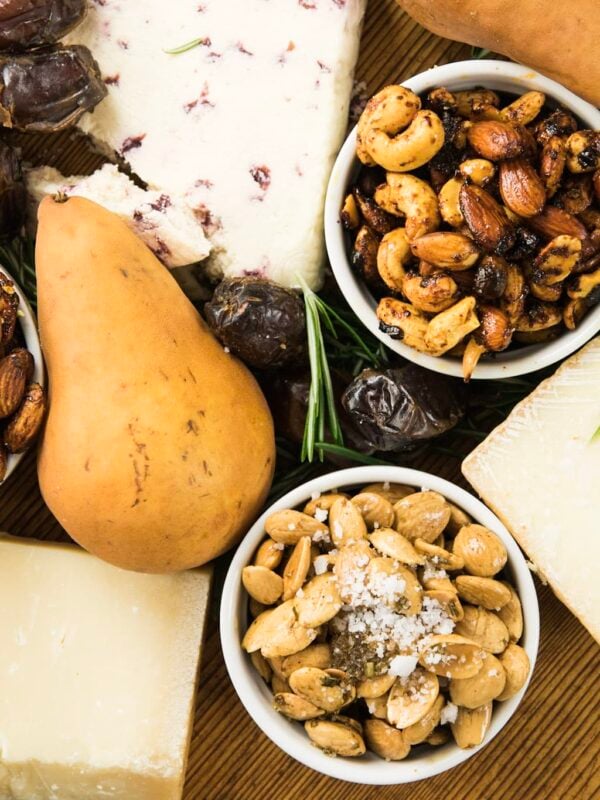 Top down view of three spiced nuts sitting on wood board with chunks of cheese, pears, and dates all around