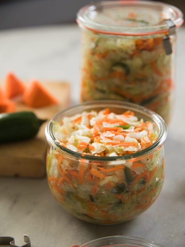 Glass Weck jar sitting on marble surface filled with pieces of carrot and cabbage with another full container in the background