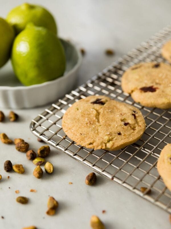 Flat shortbread cookie sitting on wire cooling rack with limes in background all on marble surface