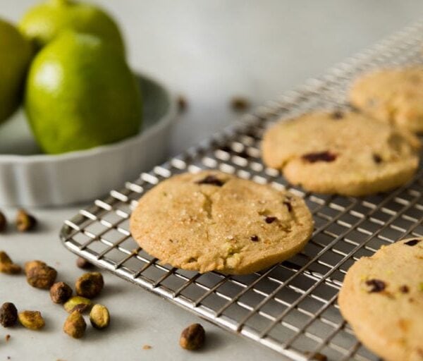 Shortbread cookie sitting on cooling rack with pistachios all around with limes in background