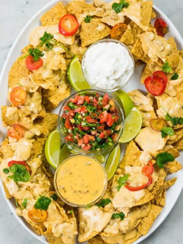Top down view of white plate filled with chips and cheese along with salsa and sour cream, shaped like a stadium