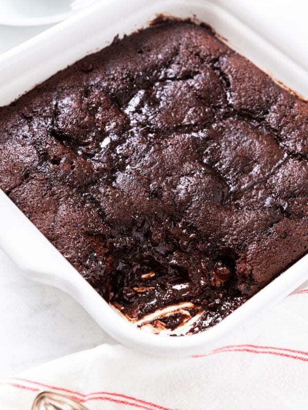 White baking dish filled with baked chocolate fudge pudding cake with scoop already taken out showing gooey interior.