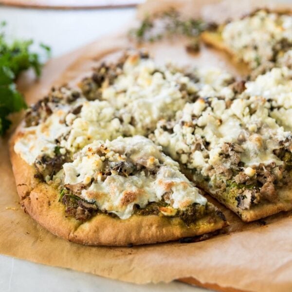 Homemade pizza crust topped with sausage, spinach, and crumbly feta cheese sitting on brown piece of parchment paper on marble surface after coming out of the oven