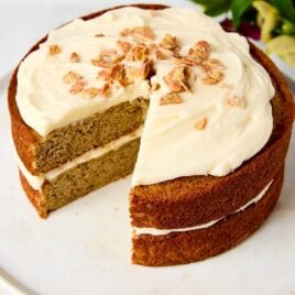 White cake stand with brown butter banana cake with two slices removed showing interior texture.