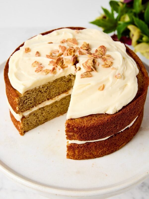 White cake stand with brown butter banana cake with two slices removed showing interior texture.