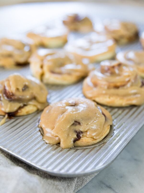 Silver muffin tin filled with cinnamon roll muffins swirled with cinnamon and glazed with a brown sugar icing