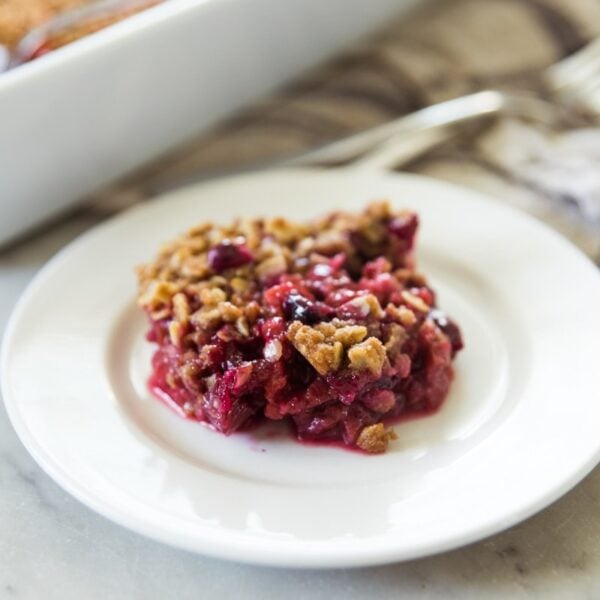 White plate with rhubarb and berry crisp sitting on marble surface with rest of baking dish in background