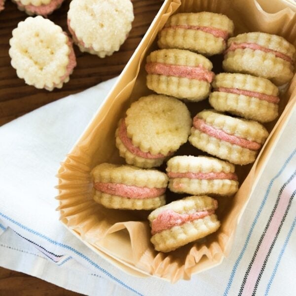 Top down view of rhubarb wafer cookies with light pink filling sitting in a parchment lined treat box one top of white dish towel