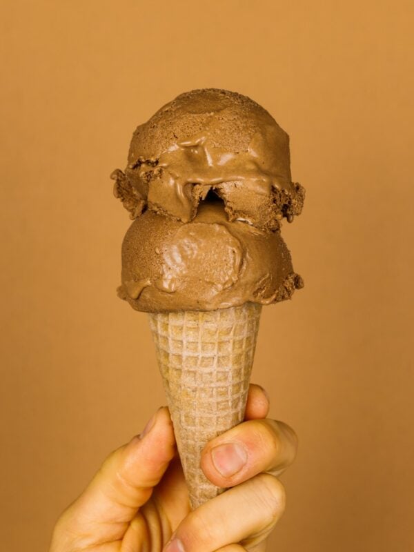 Two scoops of French silk pie ice cream on an ice cream cone held by a hand with a brown background