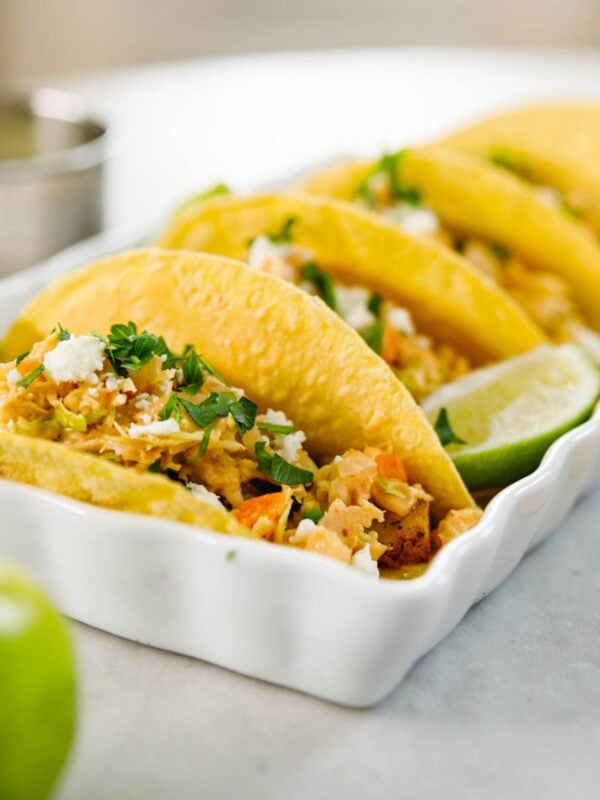 Corn tortillas filled with chickpea mixture and topped with chipotle slaw and cilantro sitting in white serving container all on marble surface