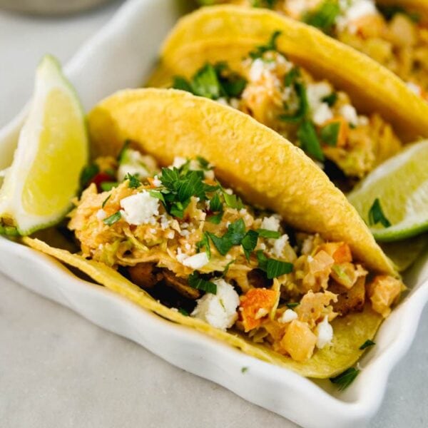 Chickpea tacos sitting in white serving container with lime wedge on each side all on marble surface and topped with chipotle slaw and cilantro