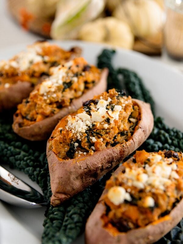 Twice baked sweet potatoes on bed of kale sitting on white plate with white pumpkins in background on white surface