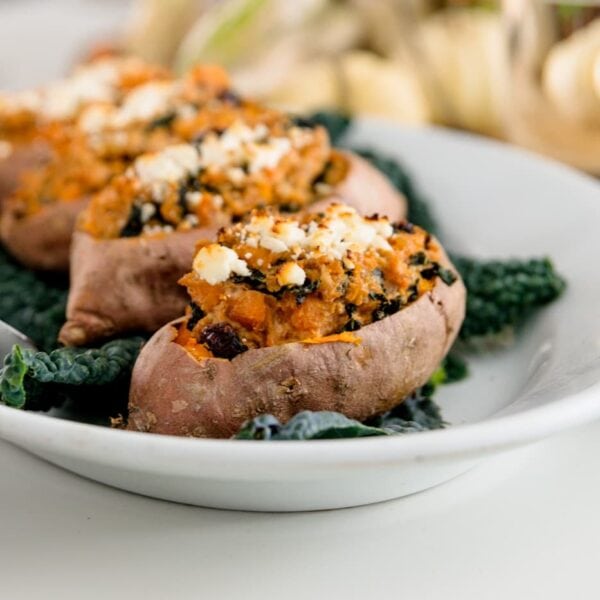 Twice baked sweet potatoes on bed of kale sitting on white plate with white pumpkins in background on white surface