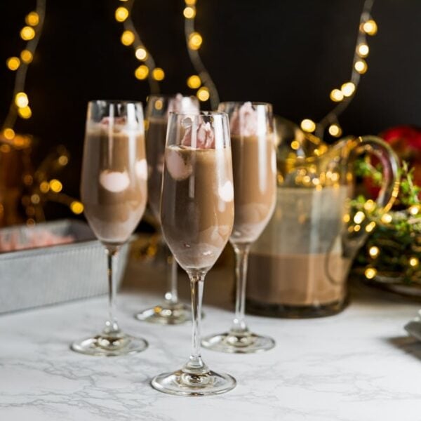 Three champagne flutes filled with pink peppermint ice cream and chocolate coffee mixture sitting on marble surface with Christmas lights on black background