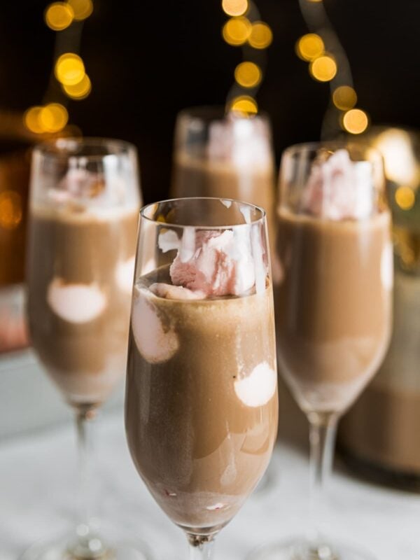 Four champagne glasses filled with chocolate mixture with pink ice cream floating all with black background with twinkling Christmas lights