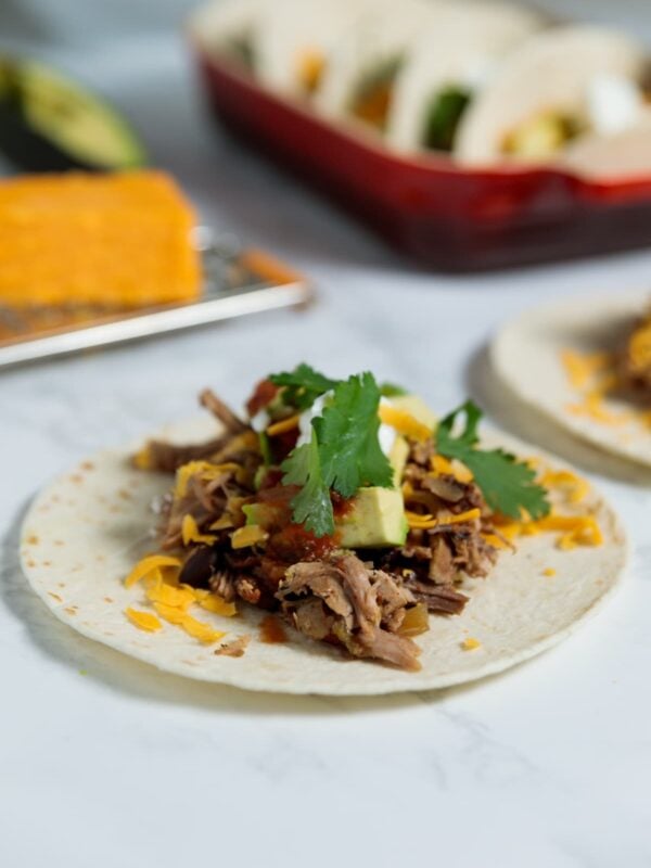 Carnitas meat on a flour tortilla with cheese, cilantro, and more on top.
