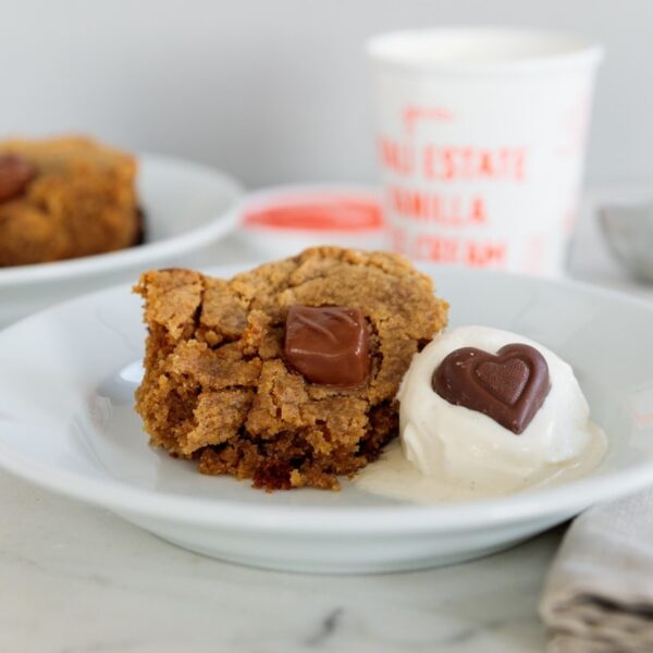 White plate with peanut butter cake with a scoop of vanilla ice cream to the side with a chocolate heart.