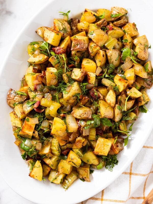 White serving platter filled with gold colored roasted potatoes with herbs sprinkled all over the top all on marble surface.