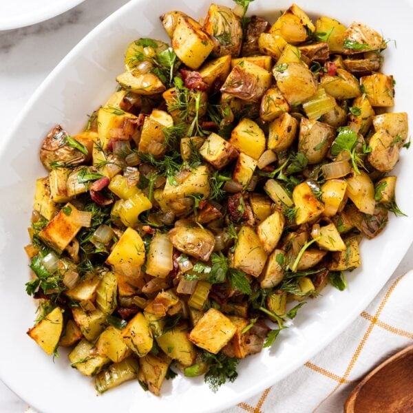 White marble surface with white platter filled with roasted German potato salad topped with herbs.