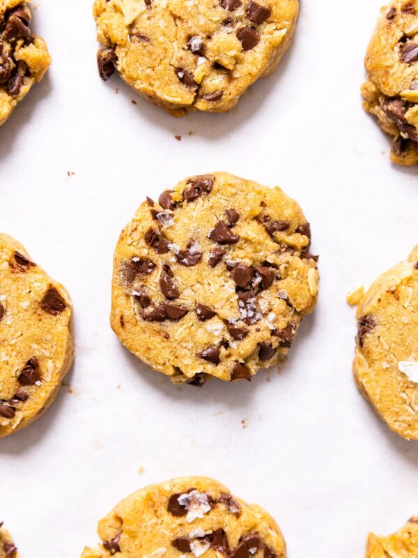 Top down view of circular light brown cookies with chocolate chips and sea salt sitting on white parchment paper