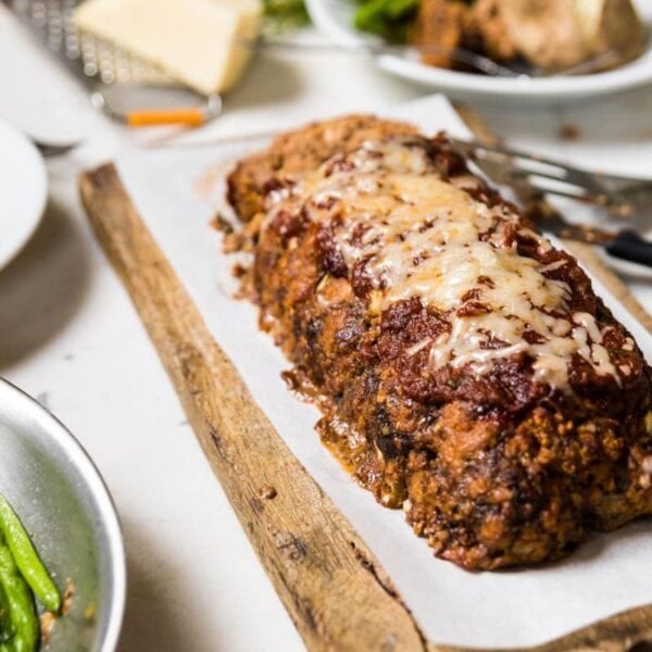 Pizza meatloaf on piece of parchment paper on a cutting board with green beans to the side.