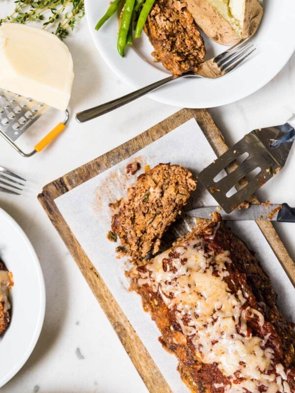 Pizza meatloaf on a cutting board with slices cut and served on plates.