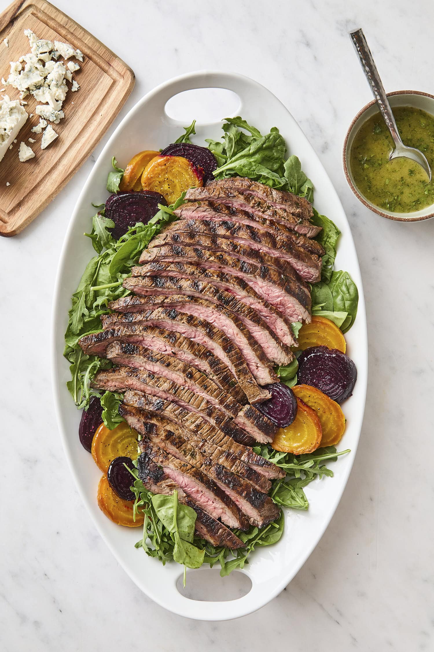 White platter with assembly of steak and beet salad on spinach and arugula.