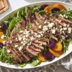 White platter with steak and beet salad with crumbled blue cheese and dressing on top.