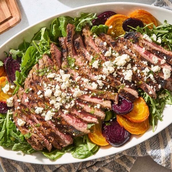 White platter with steak and beet salad with crumbled blue cheese and dressing on top.