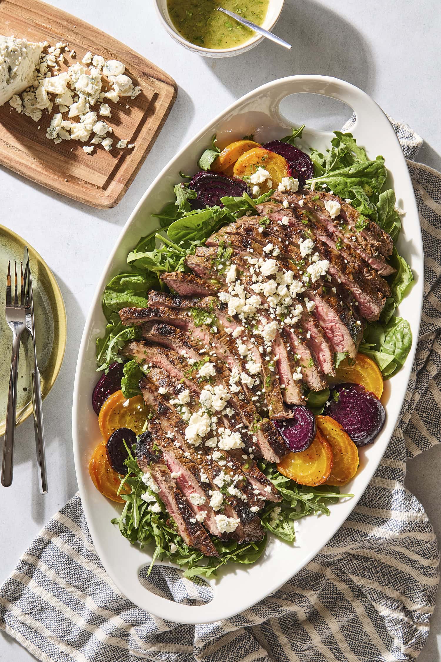 Grilled steak and beet salad with crumbled blue cheese on top with plates to the side.