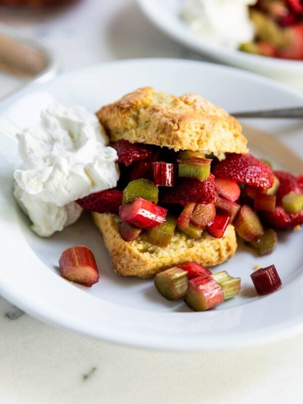 Strawberries, rhubarb and whipped cream on a bowl sandwiched between two golden biscuits on a marble surface