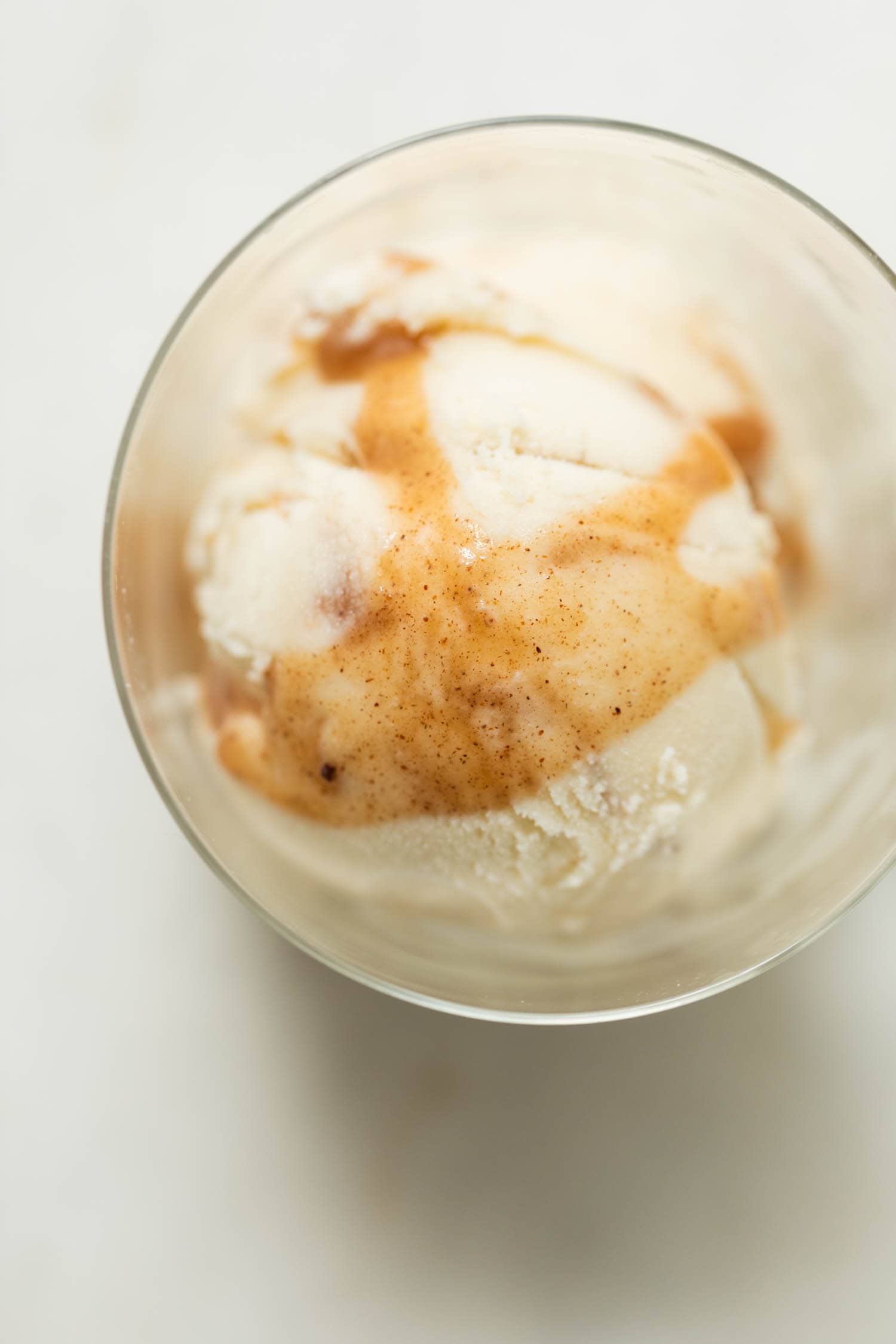 Top down view of French toast ice cream drizzled with extra cinnamon sauce in a clear glass on a marble surface