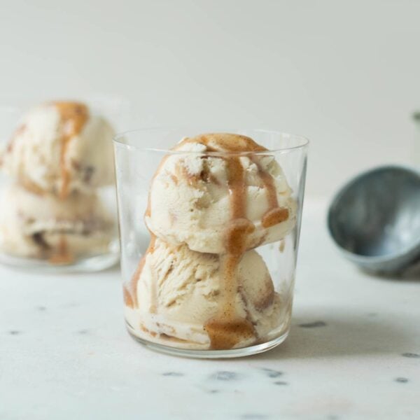 French toast ice cream drizzled with extra cinnamon sauce in a clear glass on a marble surface with second ice cream cup and ice cream scoop in background