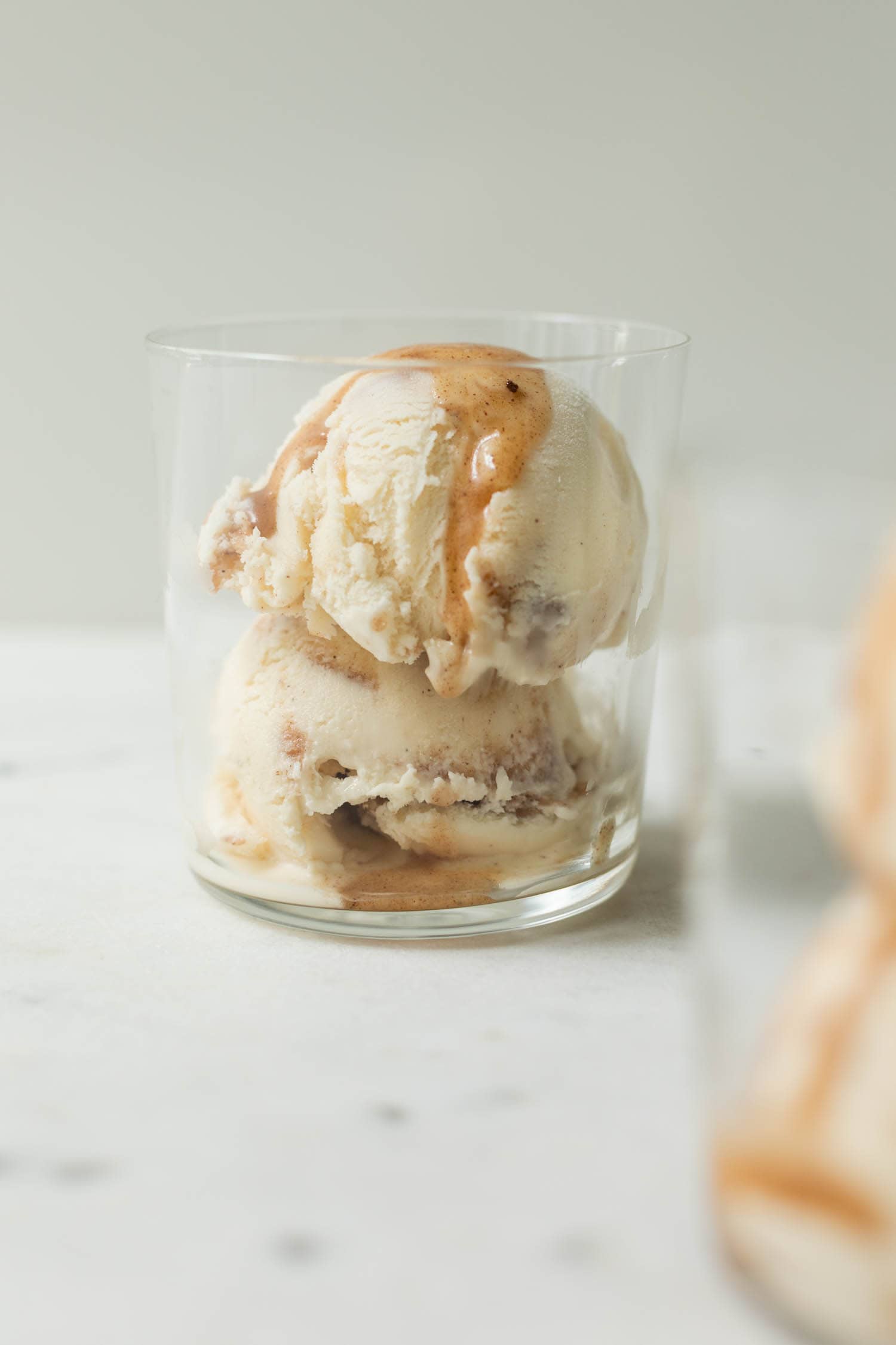 French toast ice drizzled with extra cinnamon sauce in a clear glass on a marble surface with second ice cream cup in foreground