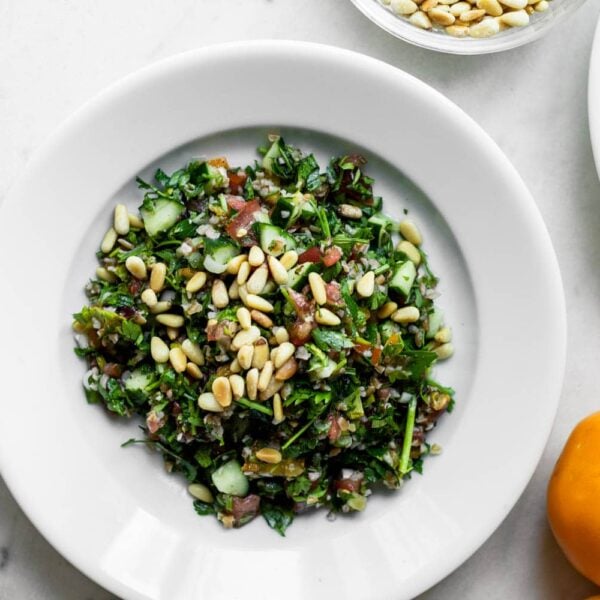 Top down view of greens sitting on white plate topped with pine nuts all on white marble surface