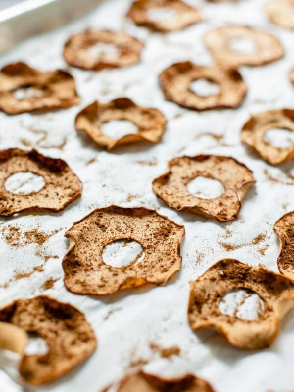 Homemade apple chips sitting on parchment-lined baking sheet on a gray slate surface